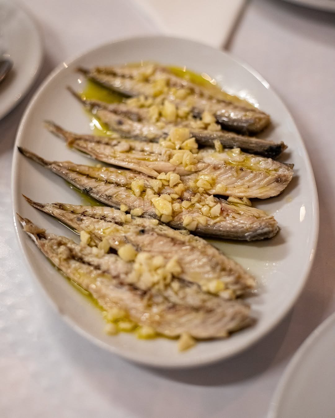 Travessa oval com sardinhas grelhadas, cobertas de alho picado e azeite