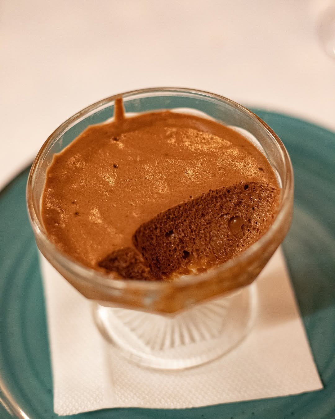Taça de vidro com mousse de chocolate, sobre um guardanapo branco e um prato verde
