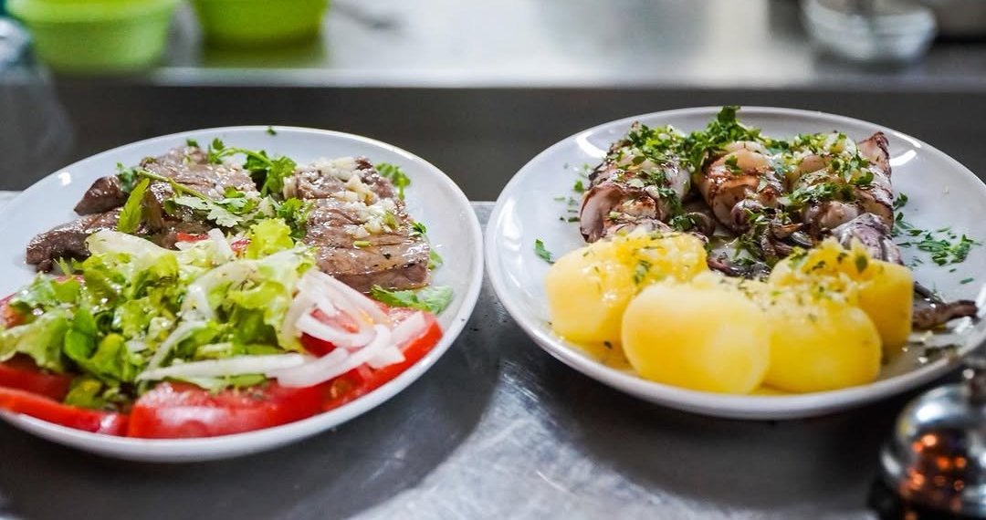Dois pratos lado a lado: barriga de atum grelhada com salada de alface, tomate e cebola, e lulas grelhadas com batata cozida e salsa